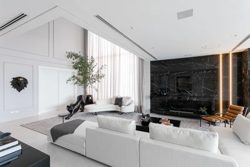 Living branco com painel de mármore preto e poltrona de couro caramelo